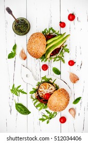 Two Veggies Burgers Served On Cutting Board Over White Rustic Table. Vegan Grilled Eggplant, Arugula, Sprouts And Pesto Burger. Veggie Beet And Quinoa Burger With Avocado. Top View, Overhead, Flat Lay