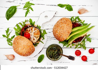 Two Veggies Burgers Served On Cutting Board Over White Rustic Table. Vegan Grilled Eggplant, Arugula, Sprouts And Pesto Burger. Veggie Beet And Quinoa Burger With Avocado. Top View, Overhead, Flat Lay