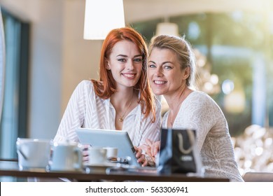 Two very beautiful women, a mother and her daughter sitting in a cafe using a digital tablet. One is blonde and the other is redhead. Shot with flare