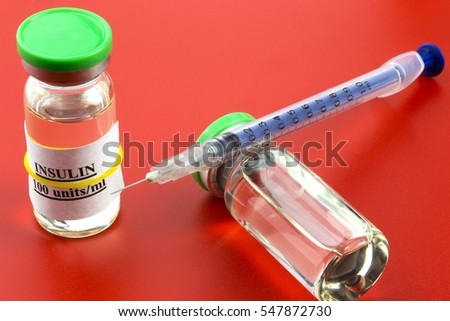Two vials with insulin hormone and  single use insulin syringe (pen) lying on the ampule. Set for diabetic. Red background.
