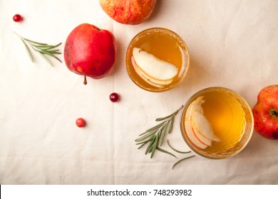 Two vintage glasses with apple cider on black background. Christmas beverages concept. Two red apples and rosemary sprig aside.  Warm backlight. Top view.