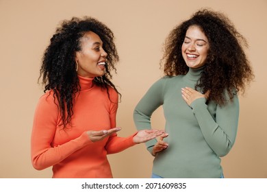 Two vivid laughing young curly black women friends 20s wearing casual shirts clothes look at each other speak communicate discuss something isolated on plain pastel beige background studio portrait