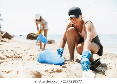 Two volunteer woman cleaning the sea beach by collecting garbage into plastic bag. - Powered by Shutterstock