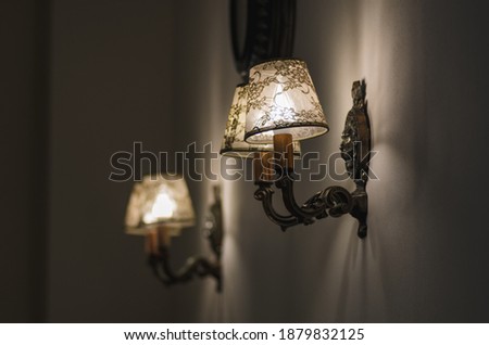 Two wall lights hang on a light-colored wall. Yellow lights in the shade. Evening, the lights are on.