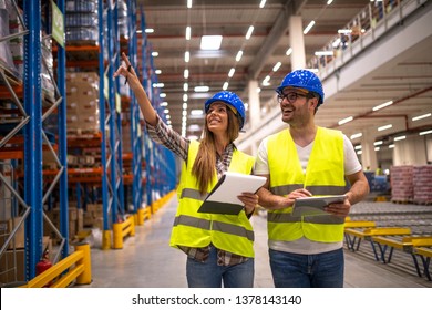 Two Warehouse Managers In Protective Work Wear Organizing Distribution In Warehouse Storage Area.