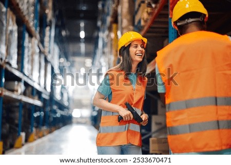 Two warehouse workers from different backgrounds share a joyful moment while scanning inventory. Uniformed and safe, they collaborate efficiently using technology for order fulfillment