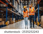 Two warehouse workers walking and talking in aisle filled with boxes, showcasing teamwork and communication in fast paced industry setting