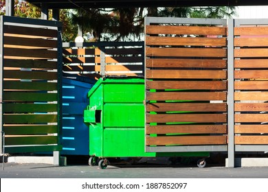 Two waste management blue and green garbage containers dumpsters in garbage enclosure used for commercial and residential garbage.