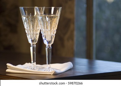 Two Waterford Lead Crystal Champagne Glasses On A Dark Wooden Table.