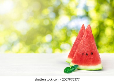 Two watermelon slice and mint leaves on wooden table top on blurred green background of lush tree leaves and sunlight. Stand counter for summer product display or visual layout design.