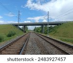 Two way railway tracks and bridge. Two railroad tracks. Concrete bridge. Cloudy day. Countryside. Field and trees.	