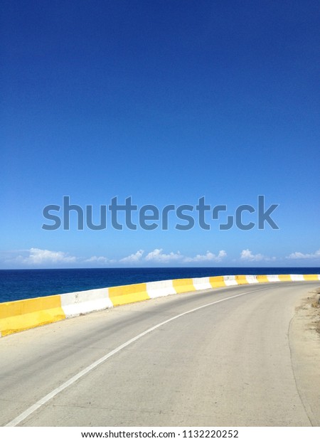 Two way road with\
concrete fence at the edge of the ocean. Barrier, guard rail,\
designed to prevent the exit of the vehicle from the curb, moving\
across the dividing strip.