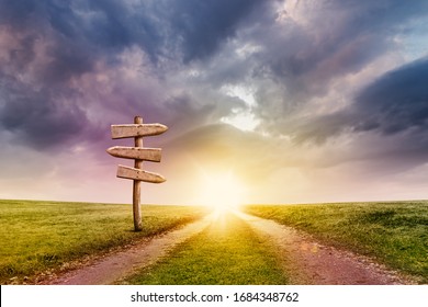 Two Ways Path on Field with Old Weathered Wood Signpost on Sunrise Sky Background