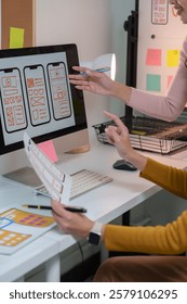Two web designers are discussing user interface of mobile application displayed on desktop computer while working together in modern office