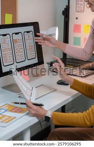 Two web designers are discussing user interface of mobile application displayed on desktop computer while working together in modern office