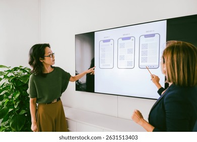 Two web designers pointing at wireframes displayed on a digital screen during a productive office meeting, collaborating on user interface and user experience design