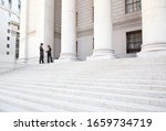 Two well dressed professionals in discussion on the exterior steps of a courthouse. Could be lawyers, business people etc.
