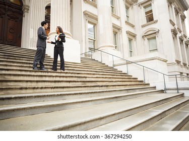 Two well dressed professionals in discussion on the exterior steps of a building. Could be lawyers, business people etc.