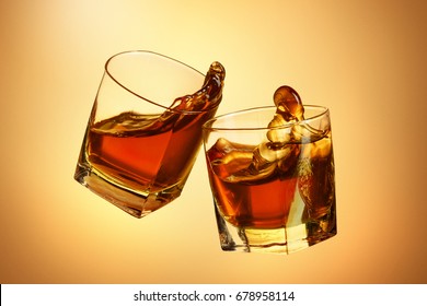 Two Whiskey Glasses Clinking Together On Brown