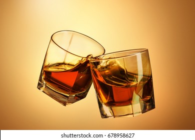 Two Whiskey Glasses Clinking Together On Brown