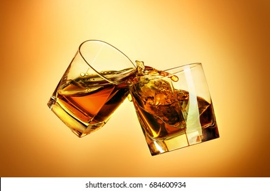 Two Whiskey Glasses Clinking Together On Brown