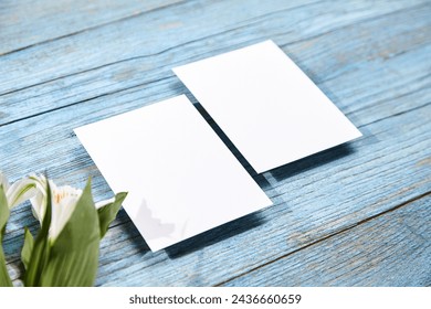 Two white blank card mockups lying parallel on a textured blue wooden surface, flanked by delicate white Alstroemeria flowers - Powered by Shutterstock