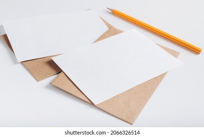 Two White Blank Paper Card Mock Up. Postcards With Empty Space, Envelopes And Pencil On White Table.