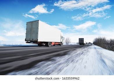 Two white box trucks with space for text on the countryside winter road in motion with snow against a blue sky with clouds
