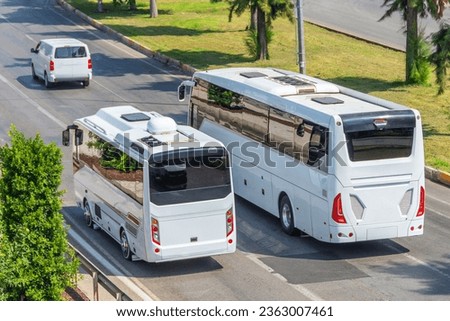 Two white buses, a large and a small one, travel opposite each other along the lanes, overtaking cars, aerial top view. Trip and journey by vehicle.