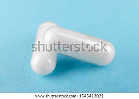 two white capsules of nutritional supplement msm, sulfur on blue background