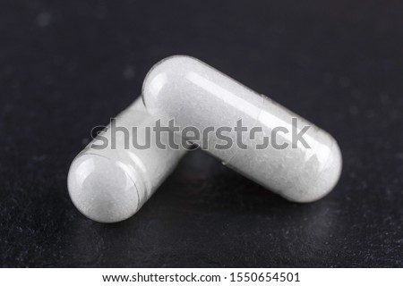 two white capsules of nutritional supplement msm, sulfur on black background
