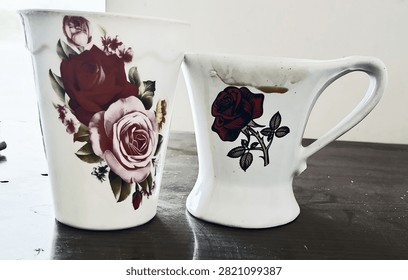 Two white ceramic mugs featuring vibrant red and pink rose floral prints resting together on a tabletop surface