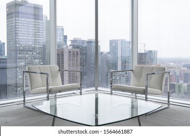 Two white chairs and a glass table in a clean, modern space with concrete floors and large windows with city views.