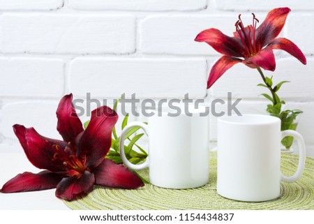 Two white coffee  mug mockup with couple of dark burgundy lily.  Empty mug mock up for design promotion.   