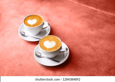 Two white cups of tasty cappucino with love art latte. Valentine's concept. Coral color backdrop.
