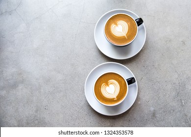 Two white cups of tasty cappucino with heart art latte. Concrete grey backdrop.