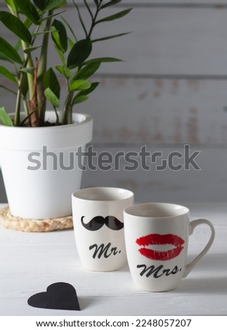 Two white cups that together form a pair. One shows a woman's red lips, and the other a man's black mustache. Good mood for Valentine's Day