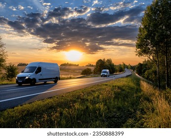 Two white fast delivery vans driving on the asphalt road in rural landscape at sunset with dark cloud - Powered by Shutterstock