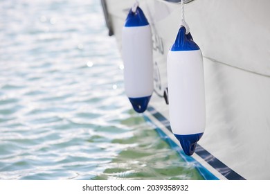 Two white fenders suspended between a boat and dockside for protection. Maritime fenders