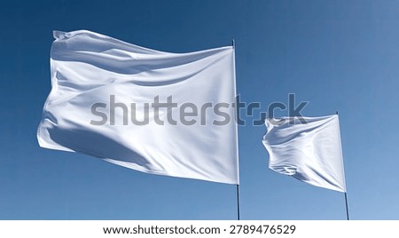 Two white flags, one large and one small, are captured mid-air, their fabric rippling dynamically in the wind against a serene, cloudless blue sky.