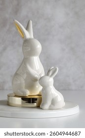 Two white and gold ceramic easter bunnies sitting on a round white table against a gray background