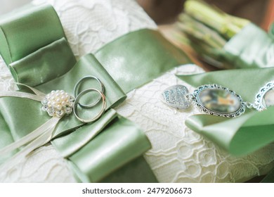 Two white gold wedding rings on a pillow with green ribbon, on a wooden table. Wedding details - Powered by Shutterstock