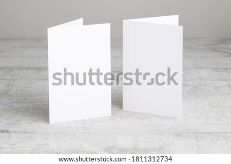 Two white greeting cards mockup, standing upright on a white wooden desk. Blank, closed cards template. 