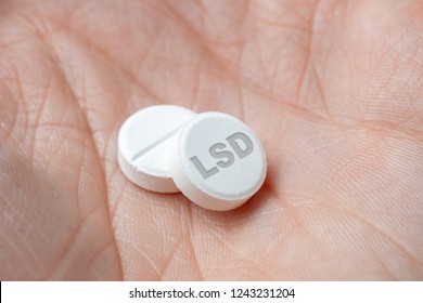 Two white LSD pills drugs in hand. closeup