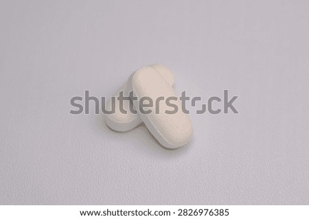 Two white oblong pharmaceutical tablets overlapping on a clean light background, illustrating medication, dosage, healthcare, and pharmaceutical concepts.