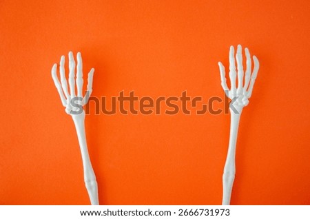 Two white plastic skeleton hands raised on orange background, Halloween or horror-themed concept with minimal design