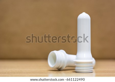 Two white preforms stand in front of brown and dirty background. These preforms made from plastic PET.