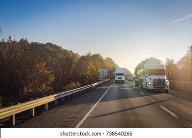 Two White Semi Tractor Trailer Trucks On The Highway At Sunrise