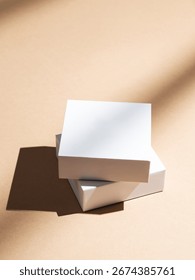Two white square boxes on a beige background with natural light and shadows. Minimalistic packaging concept or mockup for product advertising. Top view, copy space.