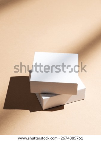 Two white square boxes on a beige background with natural light and shadows. Minimalistic packaging concept or mockup for product advertising. Top view, copy space.